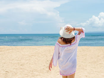 Woman wearing hat while standing on beach against sky