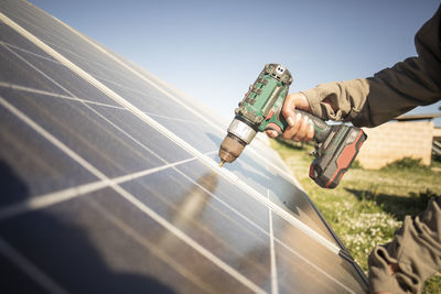 Hand of female engineer installing solar panels with drill while working at power station