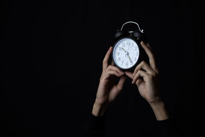 Close-up of hand holding clock over black background