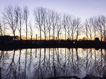 Silhouette bare trees by lake against sky during sunset