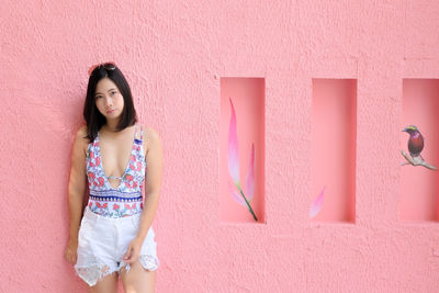 Portrait of woman standing against pink wall