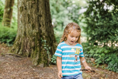 Happy woman standing by tree trunk in forest