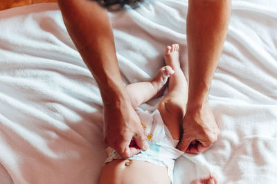 Top view of dad touching legs of newborn infant in diaper lying on bed in house