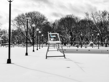 Bare trees on snow field against sky in city