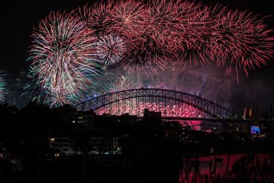 Firework display over illuminated city against sky at night