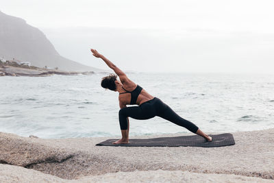Rear view of woman jumping at beach against sky