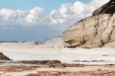 Waves at beach by mountain against sky