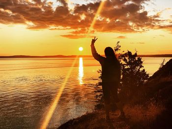 Rear view of woman standing at beach against sky during sunset