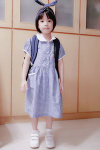 Portrait of cute girl in school uniform standing against wall