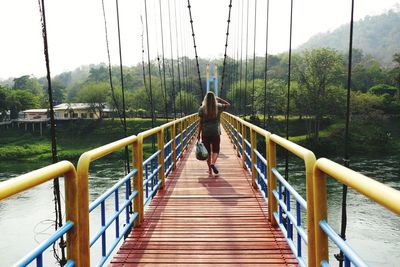 Rear view of woman walking on footbridge over lake against trees