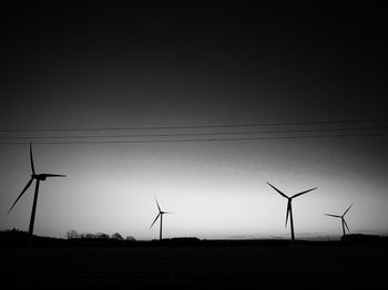 Silhouette of wind turbines on field against sky