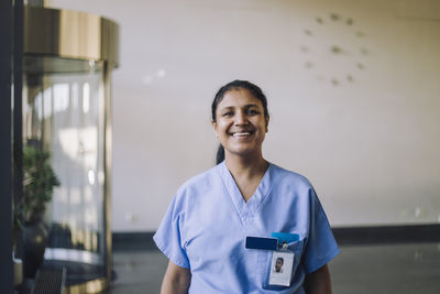Portrait of smiling female doctor in blue scrubs standing at hospital