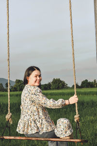 Woman sitting on swing at playground against sky