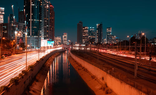 Light trails on street amidst buildings against sky at night