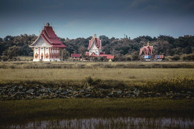 Scenic view of field by houses against sky