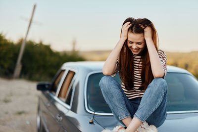 Portrait of young woman sitting on car