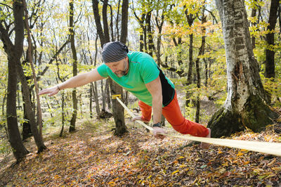 A bearded man in age balances while sitting on a taut slackline in the autumn forest. outdoor