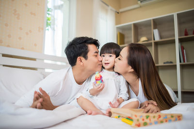 Parents kissing daughter on cheek at home