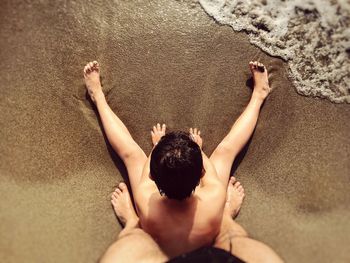 Low section of father standing behind son on shore at beach