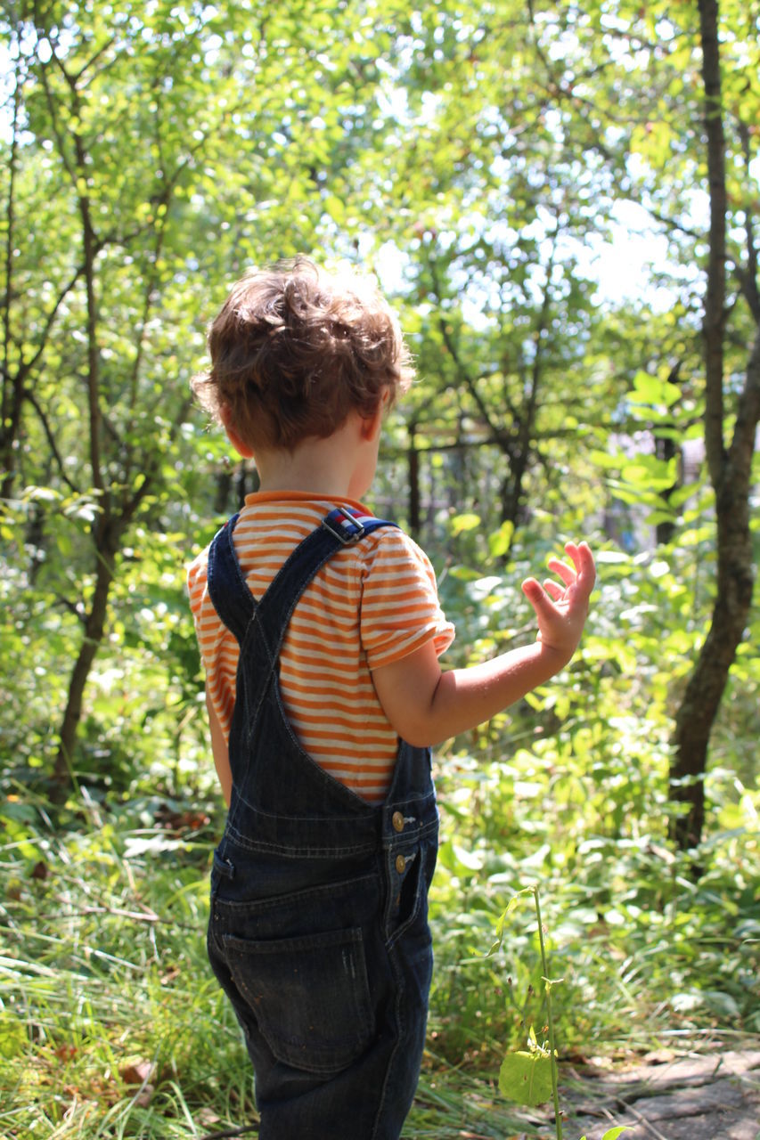 BOY STANDING IN FRONT OF TREE