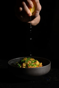 Midsection of person holding bowl against black background