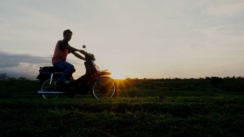 Side view of man riding motorcycle on field against sky during sunset