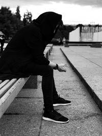 Side view of man sitting on bench in city