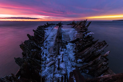 Shipwreck on sea against sky in winter during sunset
