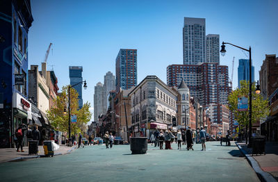 People on street amidst buildings in city against clear sky