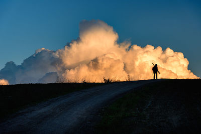 Silhouette person with tripod standing on field by cloudy sky