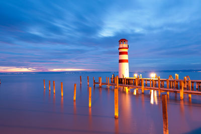 Lighthouse by sea against sky at sunset