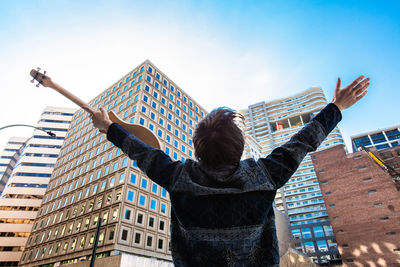 Rear view of woman standing by building against sky