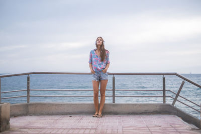 Full length of woman standing by railing against sea