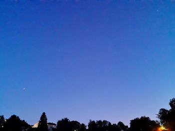 Low angle view of silhouette trees against clear blue sky