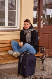 Full length of man sitting on bench with suitcase