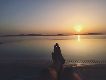 Low section of man sitting against sea during sunset