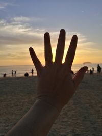 Close-up of hand against sea at sunset