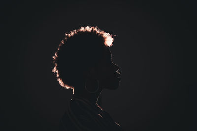 Side view silhouette of unrecognizable african american female with frizzy hair standing in darkness on black background