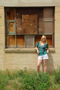 Portrait of girl standing against old abandoned building in grassy field
