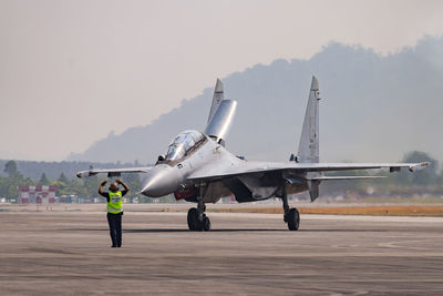 Man standing by air vehicle on runway against sky