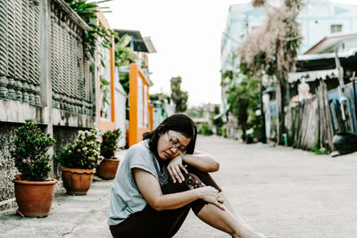 Portrait of young woman sitting on sidewalk in city