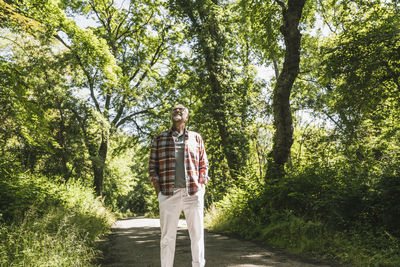 Smiling senior man standing with hands in pockets at park