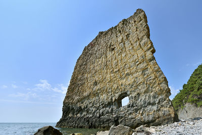 Low angle view of rock formation in sea against blue sky