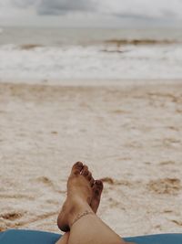 Low section of woman relaxing on beach against sky