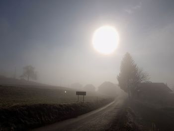 Road amidst field against sky during foggy weather