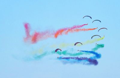 Low angle view of people paragliding with colorful smoke against clear sky