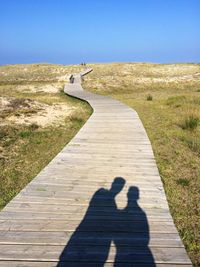 Shadow of couple amidst field on boardwalk