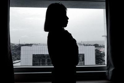 Silhouette woman looking through window in city