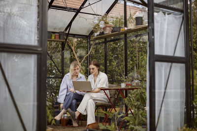 Women sitting in greenhouse and using laptop