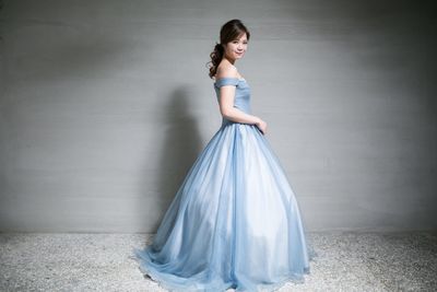Portrait of smiling young woman in dress standing against wall